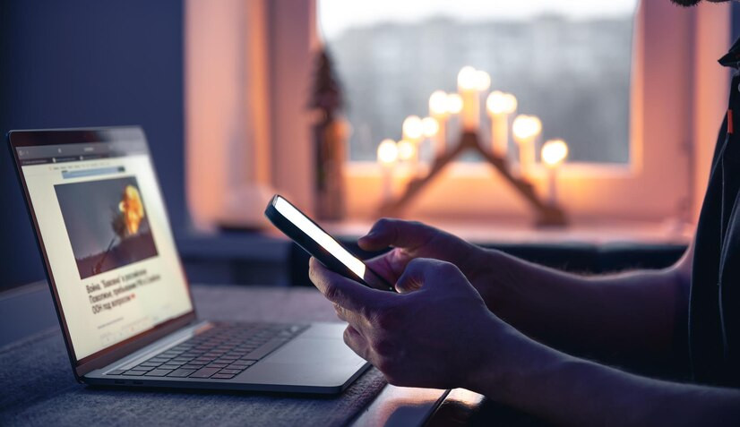 man with smartphone sits front laptop late night
